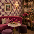 Load image into Gallery viewer, Reese Way wallpaper by Pickwick & Elm in a Palm Beach cocktail lounge featuring a curved pink velvet sofa, marble table, brass bar cabinet, and crystal glassware.