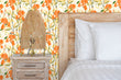 Load image into Gallery viewer, Orange cottage floral fabric peel and stick wallpaper in bedroom with bed and side table with lamp
