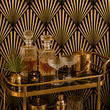 Load image into Gallery viewer, Crystal decanters and coupe glasses displayed on a brass bar cart against the bold geometric Hutton wallpaper by Pickwick &amp; Elm.
