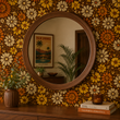 Load image into Gallery viewer, A round wood mirror creates a striking focal point against Sydney Place floral wallpaper by Pickwick &amp; Elm, bringing retro charm and warm vintage colors to this mid-century entryway.
